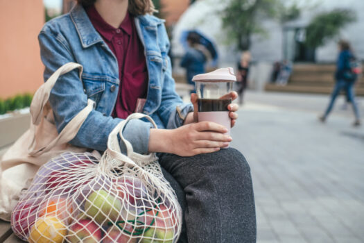 Young woman with eco-friendly reusable coffee cup and cotton bag, zero waste concept