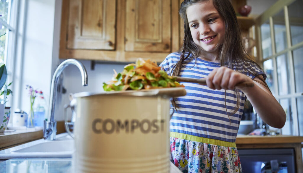 Girl In Kitchen Making Compost Scraping Vegetable Leftovers Into Bin