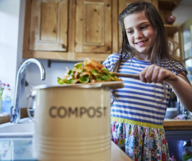 Girl In Kitchen Making Compost Scraping Vegetable Leftovers Into Bin